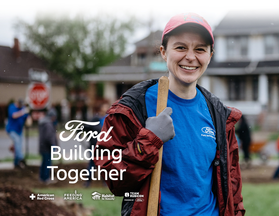 Blue shirt Ford volunteer holding a shovel smiling